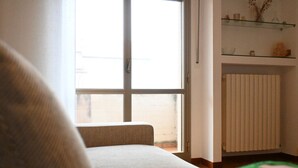 Een kamer met een bank, een raam, een radiator en planken met decoratieve objecten.
