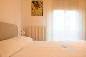 Ein Hotelzimmer mit Bett, Heizkörper, einem Bild an der Wand und einem Fenster mit Vorhängen.
