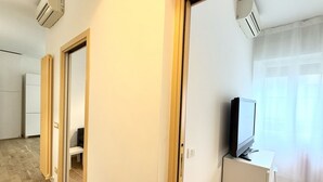 Ein Zimmer mit Fernseher auf einem Schrank, einer Tür zu einem anderen Raum und einer Klimaanlage an der Wand.