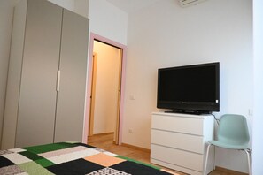 A bedroom with a bed, a television on a dresser, a chair, and a wardrobe.