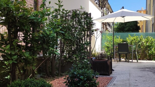 Ein Patio mit Tisch und Stühlen, ein kleiner Garten mit Pflanzen und einem Kiesweg, sowie ein Gebäude im Hintergrund.