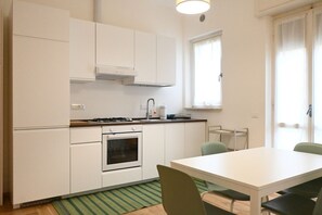 A compact kitchen with white cabinets, a stove, an oven, a window, and a dining table with chairs.