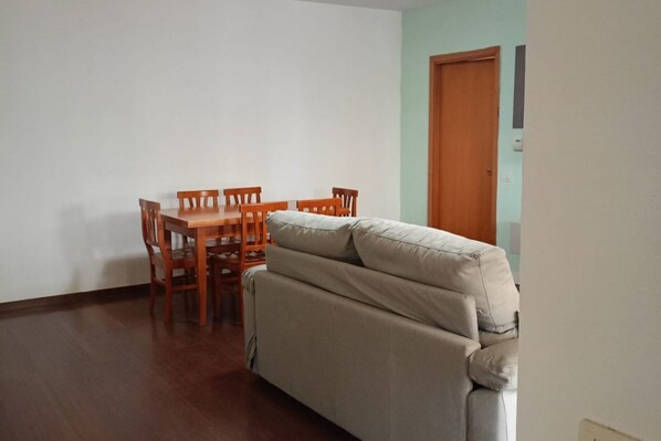 Une pièce avec une table et des chaises de salle à manger en bois, un canapé beige et une porte en bois.