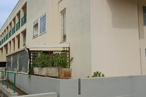 Un edificio de varios pisos con balcones, un espacio al aire libre cubierto con plantas en macetas y una escalera de hormigón.