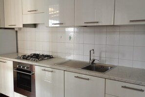 Une cuisine avec des armoires blanches, un évier en acier inoxydable et une cuisinière à gaz.