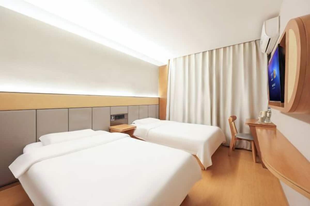 A hotel room with two beds, a desk, a chair, and a large window with curtains.