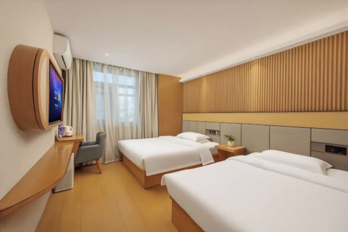 Une chambre d’hôtel avec deux lits, une télévision, un bureau et une fenêtre avec des rideaux.