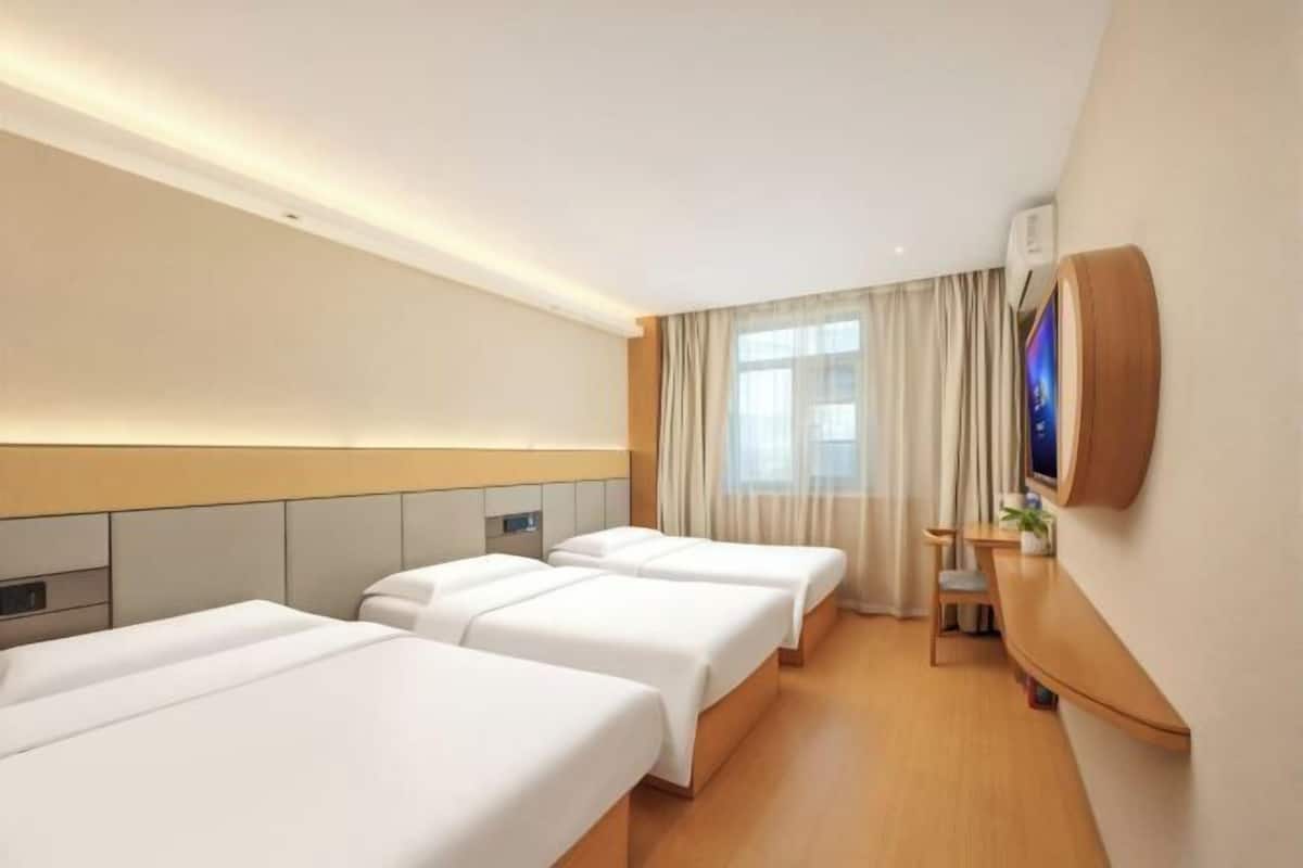 A hotel room with three beds, a wooden desk, a TV, and a window with curtains.