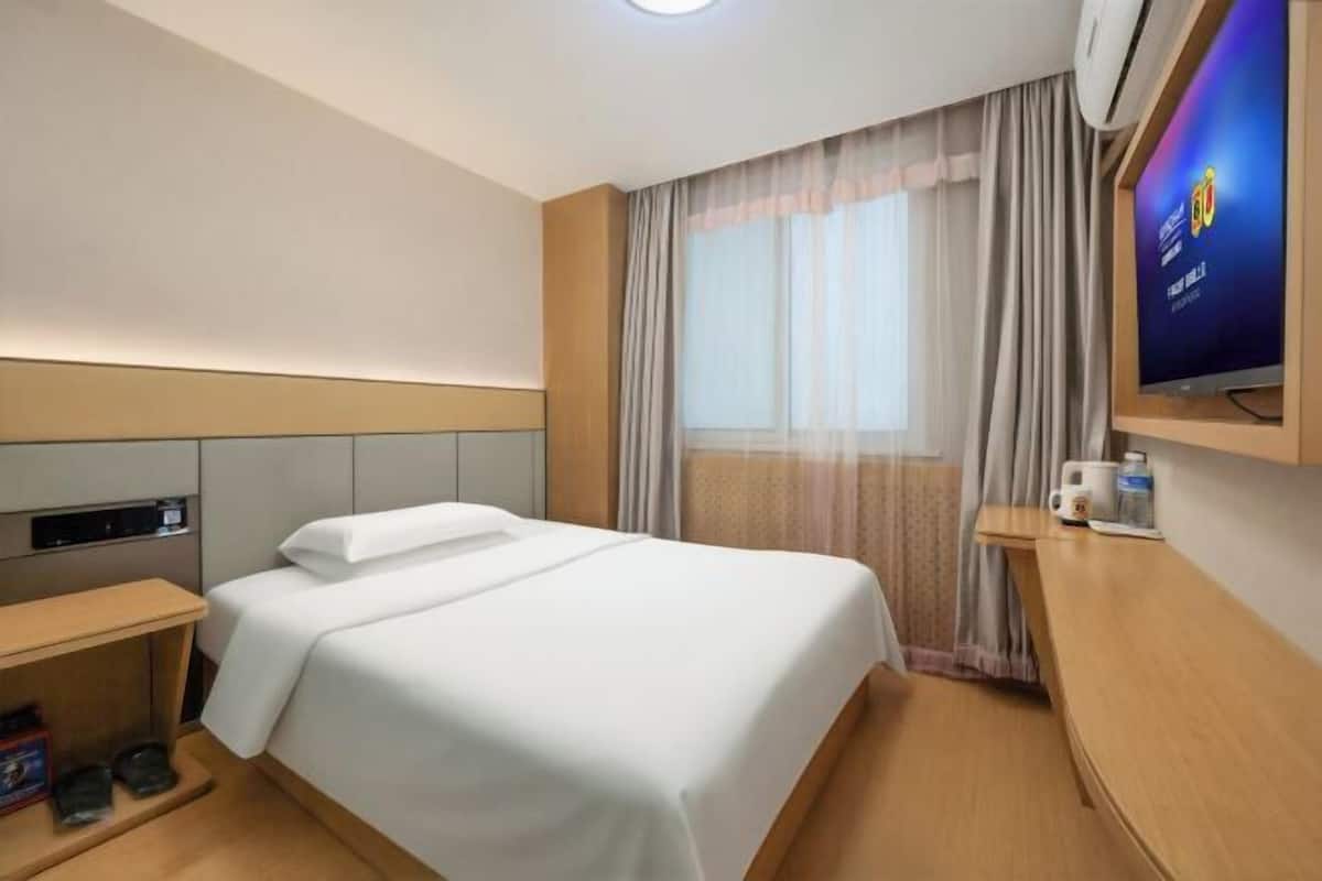 A hotel room with a bed, a TV, a desk, and a window with curtains.