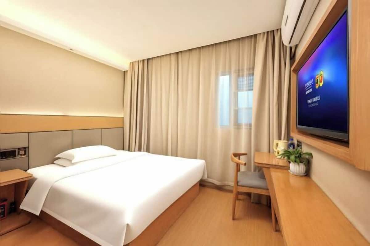 A hotel room with a bed, a desk, a chair, a television, and a window with curtains.