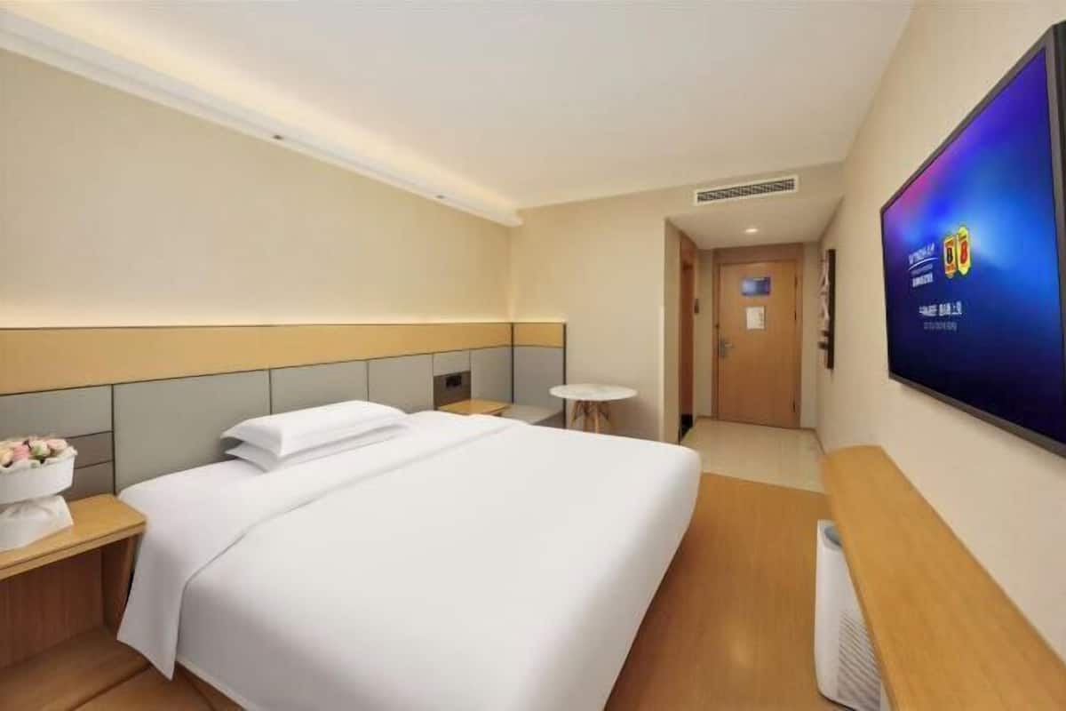A hotel room with a bed, bedside table, TV, and a small table with a vase.