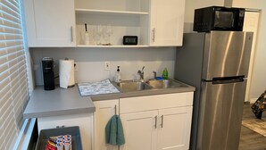 A modern kitchen with white cabinets, a stainless steel refrigerator, a microwave, a sink with a faucet, and a kettle. - Studio in The Heart of Soldotna (Soldotna)
