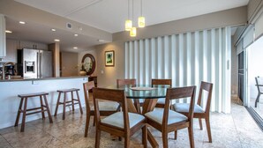 Eine moderne Küche mit Kühlschrank, Herd und Spüle. Ein Essbereich mit Glastisch und Holzstühlen ist ebenfalls vorhanden.