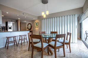 A modern kitchen with a refrigerator, stove, and sink. There is a dining area with a glass table and wooden chairs.