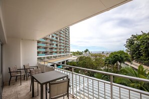 Ein Balkon mit Tisch und Stühlen, mit Blick auf ein Gebäude mit mehreren Balkonen und einer Aussicht auf Stadt und Palmen.