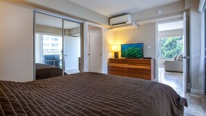 Ein Schlafzimmer mit einem großen Bett, einer Holzkommode, einem Fernseher und einer Glastür zum Balkon.
