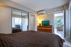 Ein Schlafzimmer mit einem großen Bett, einer Holzkommode, einem Fernseher und einer Glastür zum Balkon.