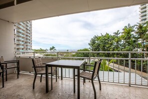 A balcony with a table and chairs, overlooking a cityscape with palm trees and a high-rise building.
