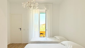 A room with two beds, a chandelier, a door, and a view of the outside. - SE156 – Senigallia, three-room apartment a few steps from the sea (Senigallia)