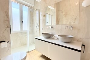 Une salle de bain moderne avec une douche à l’italienne en verre, deux vasques et un grand miroir.