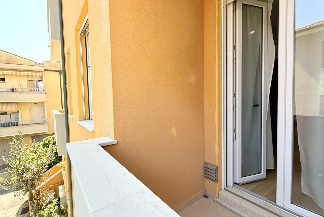 A balcony with a white railing, a sliding glass door, and a view of neighboring buildings.