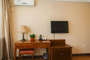 Une chambre d’hôtel avec un bureau en bois, une chaise, un téléviseur fixé au mur et une petite plante en pot posée sur le bureau.