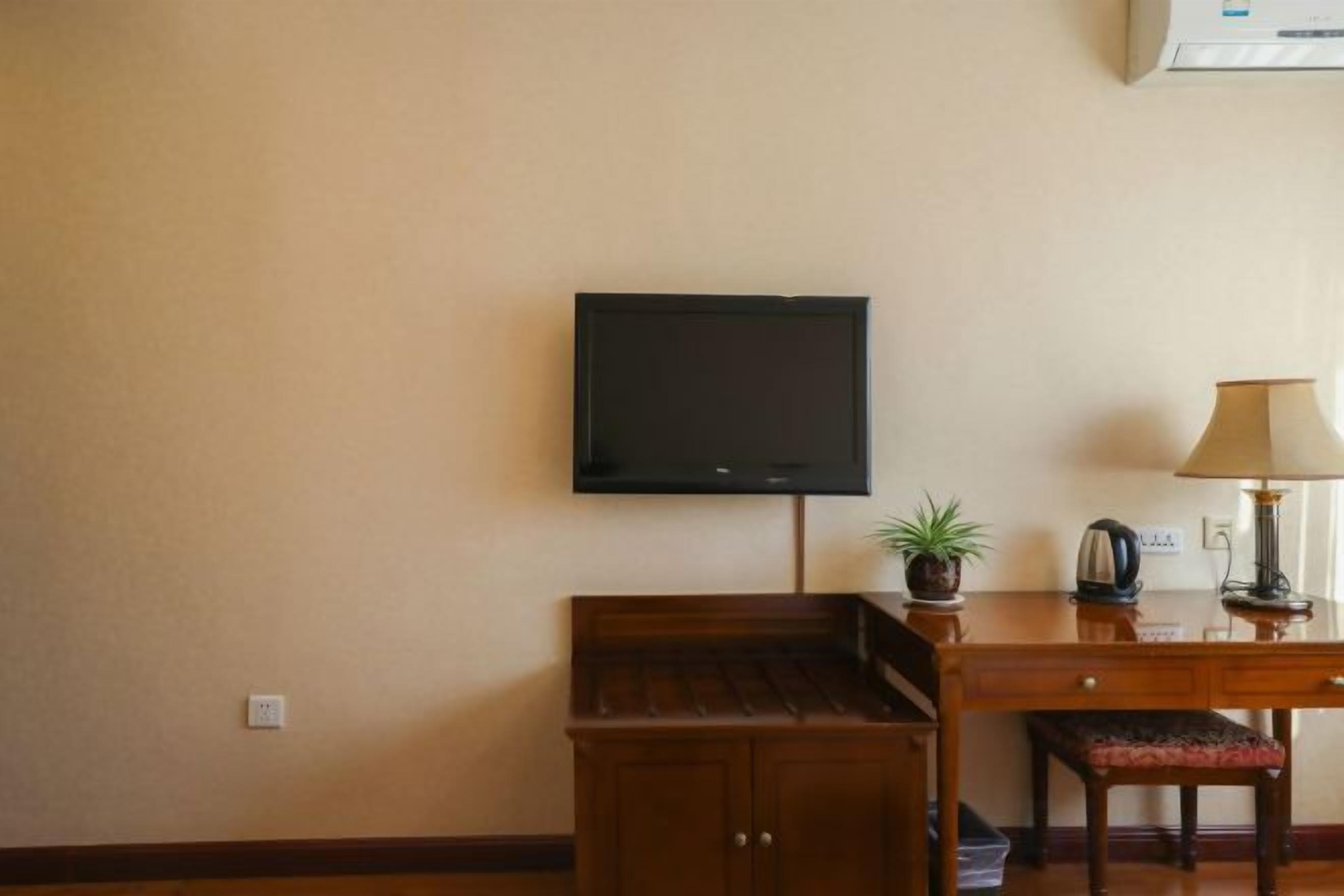 Una stanza con televisione a muro, una scrivania con lampada, una piccola pianta e una panca.