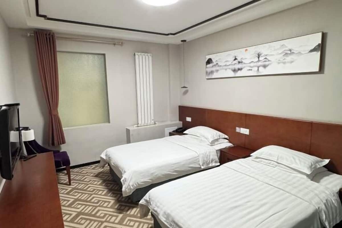 Une chambre d’hôtel avec deux lits simples, une télévision, un bureau et un tableau au mur.