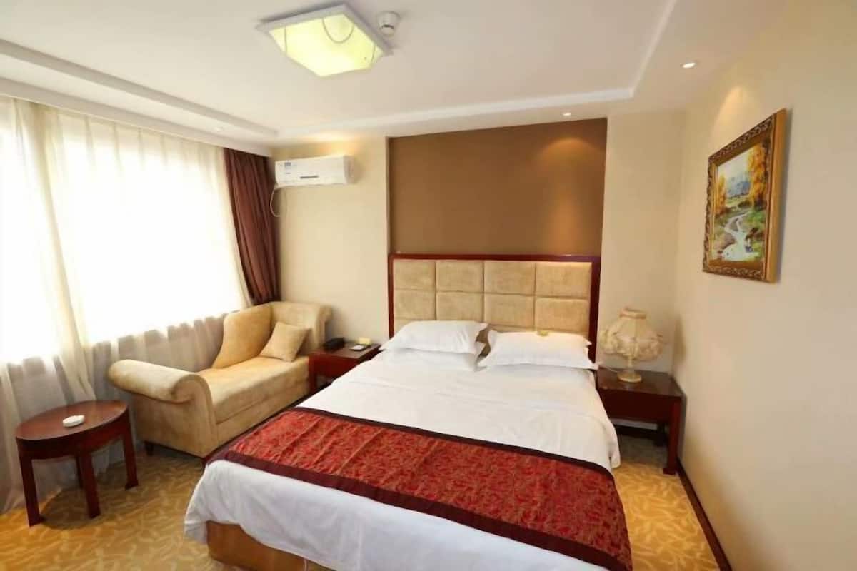 Une chambre d’hôtel avec un grand lit, un canapé, une petite table, une table de chevet et un tableau au mur.