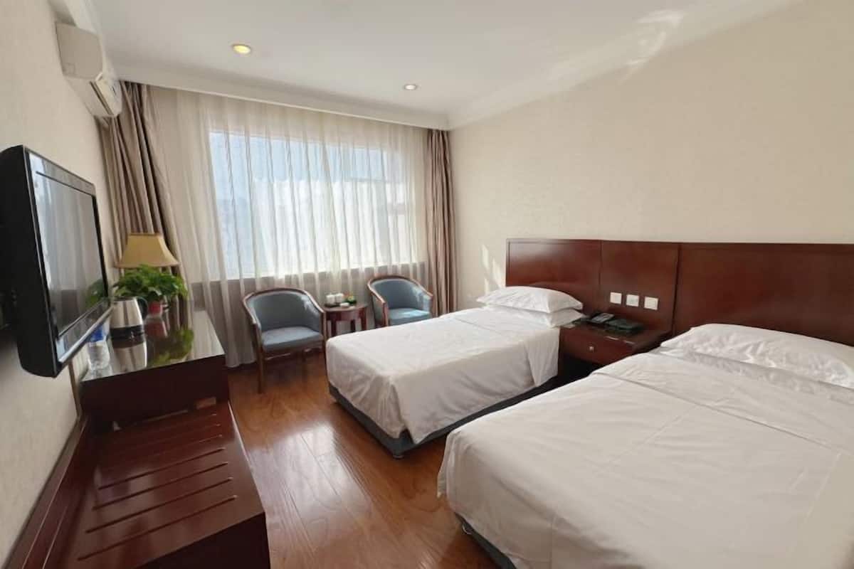 Une chambre d’hôtel avec deux lits, un bureau avec une chaise, une télévision et une fenêtre avec des rideaux.