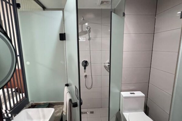 A modern bathroom with a glass-enclosed shower, a toilet, and a sink.