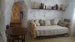A cozy room with a wooden sofa, a small round table, and a bookshelf against a white textured wall. - Cave House "La Estrella" 10 minutes from Granada center. (Monachil)