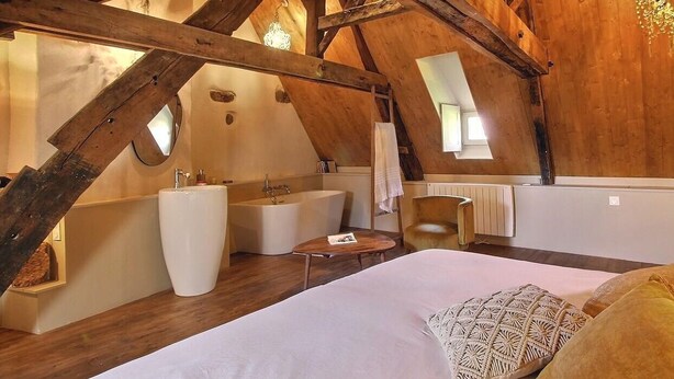 A bedroom with a large bed, a vanity with a sink, a bathtub, and a chair.