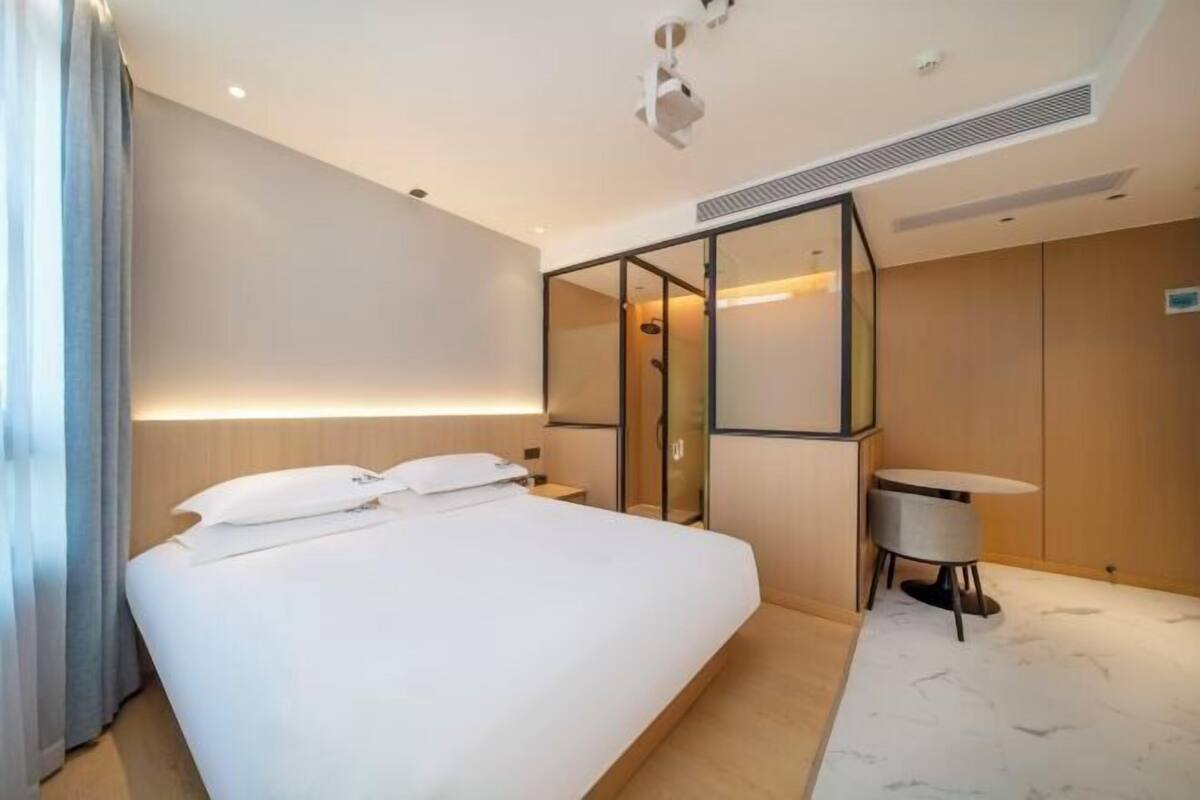 A modern hotel room with a large bed, a small desk, and a glass shower enclosure.