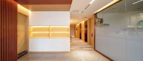 A modern hotel corridor with a reception area, wooden paneling, and a glass wall.