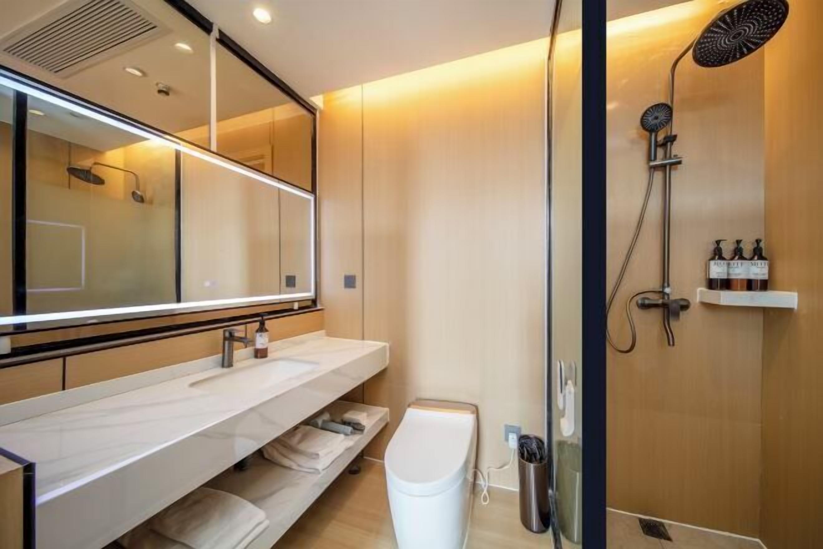 Un baño moderno con un espejo grande, ducha con cabezal de lluvia y tocador con lavabo y toallero.