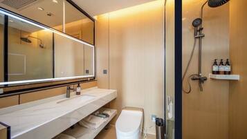 Un baño moderno con un espejo grande, ducha con cabezal de lluvia y tocador con lavabo y toallero.