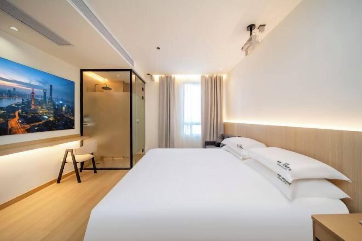 A modern hotel room with a large bed, a desk, and a cityscape painting on the wall.