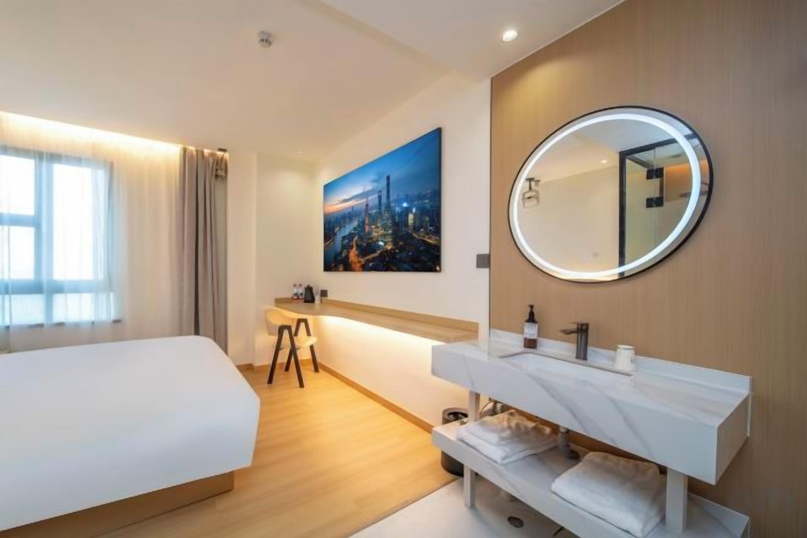 Habitación de hotel con cama, escritorio, baño con espejo y un cuadro de un paisaje urbano en la pared.