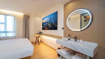 Habitación de hotel con cama, escritorio, baño con espejo y un cuadro de un paisaje urbano en la pared.