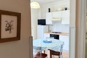 A dining area with a table and chairs, a framed artwork on the wall, and a kitchen in the background.