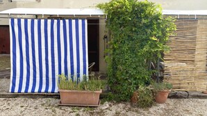 A small outdoor area with a striped fabric, potted plants, and a building in the background. - P054 - Porto Recanati, comfortable three-room apartment with outdoor patio (Porto Recanati)