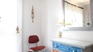 A room with a white wall, a red chair, a blue and white dresser, a lamp, and a mirror. - P054 - Porto Recanati, comfortable three-room apartment with outdoor patio (Porto Recanati)