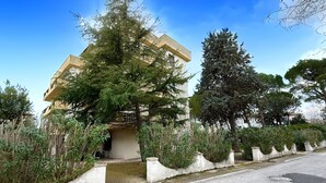 A residential building with a flat roof, surrounded by greenery and a concrete sidewalk. - P054 - Porto Recanati, comfortable three-room apartment with outdoor patio (Porto Recanati)