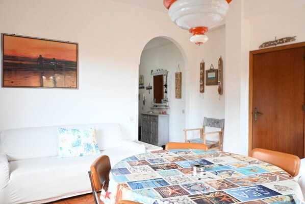 A room with a round table covered with a collage of images, a white sofa, a wooden door, and a painting on the wall.