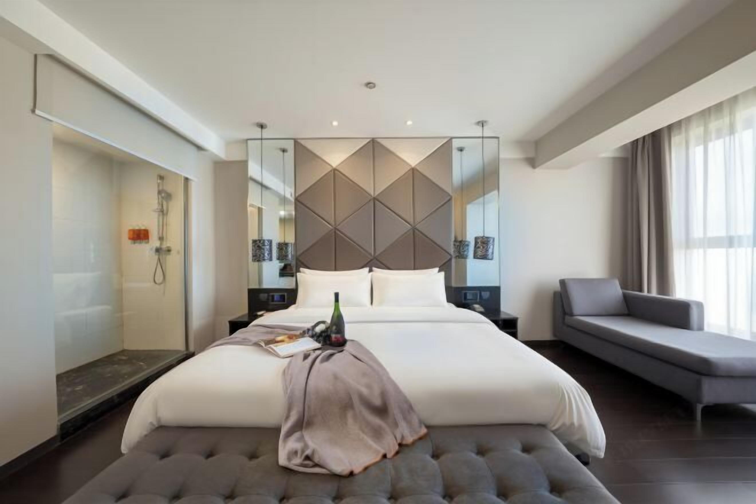 A modern hotel room with a large bed, a seating area, and a shower.