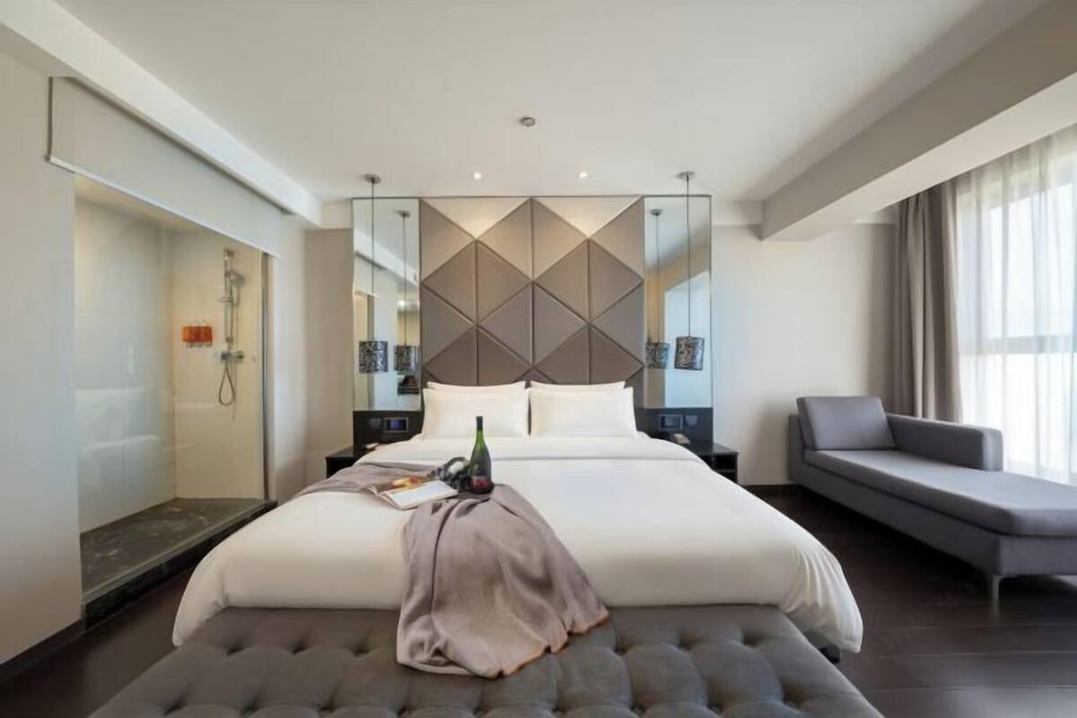 A modern hotel room with a large bed, a seating area, and a shower.