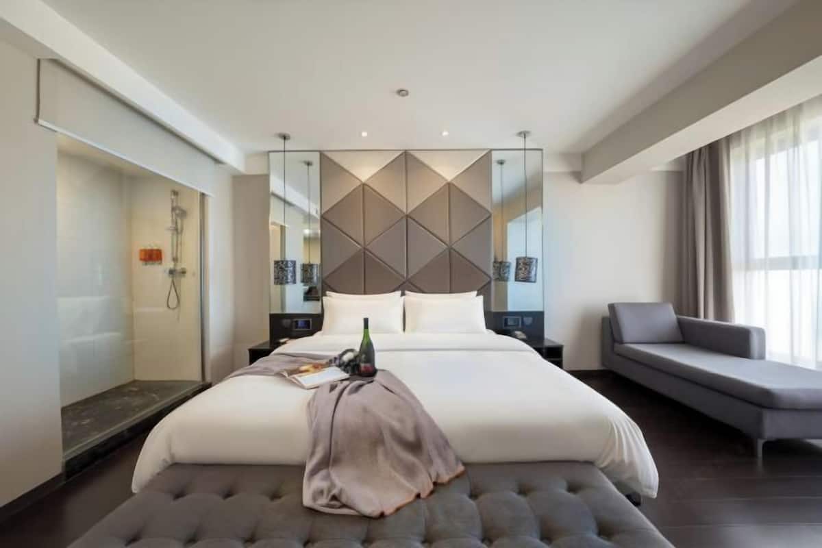 A modern hotel room with a large bed, a seating area, and a shower.