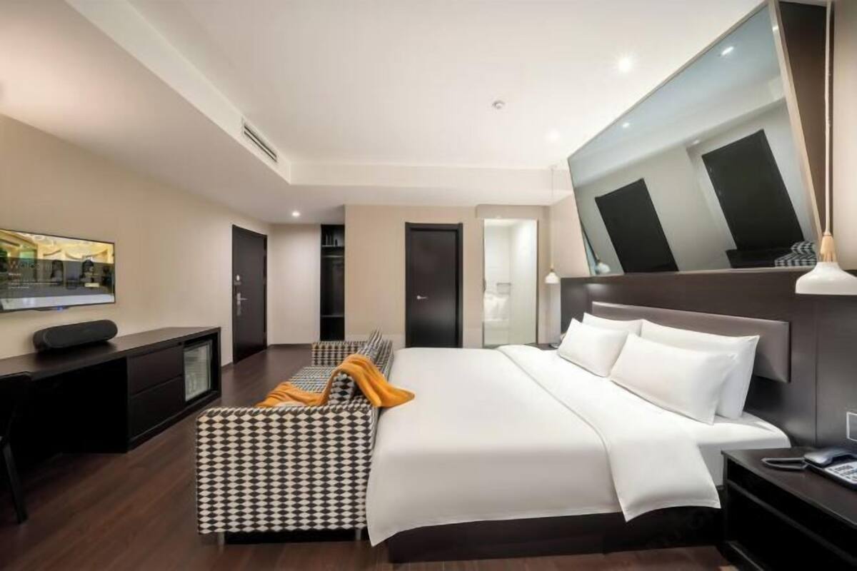 A modern hotel room with a large bed, a desk, a chair, a TV, and a mirror.