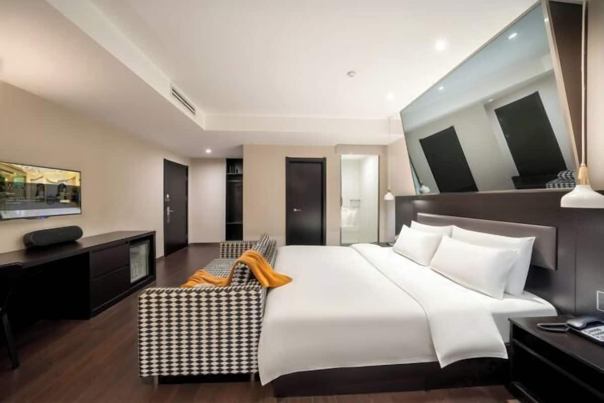A modern hotel room with a large bed, a desk, a chair, a TV, and a mirror.